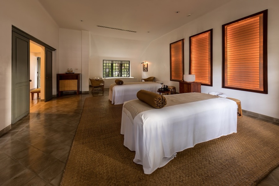 Massage table dressed in white linens with frangipani flowers